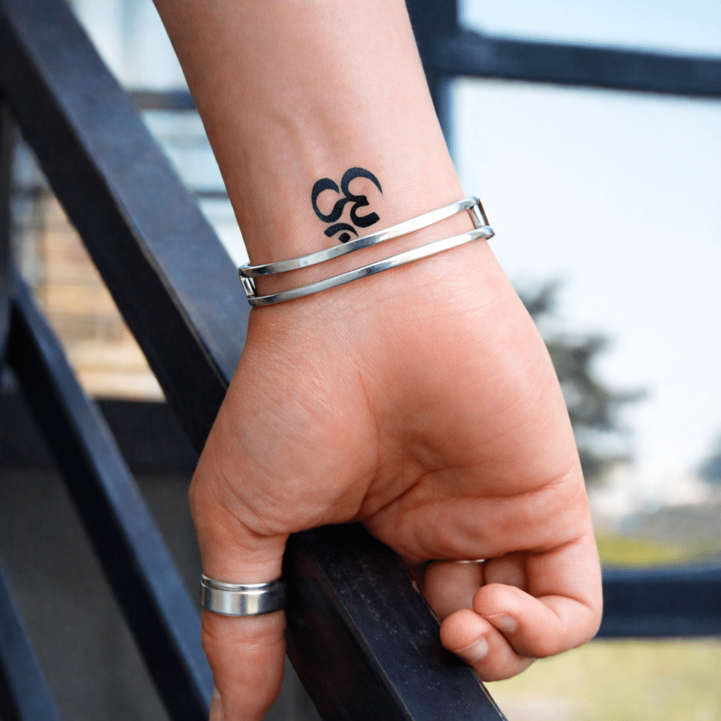 Tatouage éphémère au jagua bleu foncé représentant le symbole Om, de petite taille, appliqué au-dessus du poignet