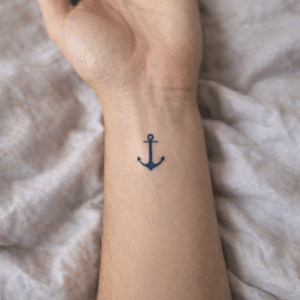Tatouage éphémère au jagua bleu foncé représentant une ancre marine, de petite taille, appliqué au centre du poignet, avec un rendu réaliste épousant le grain et les reliefs naturels de la peau.